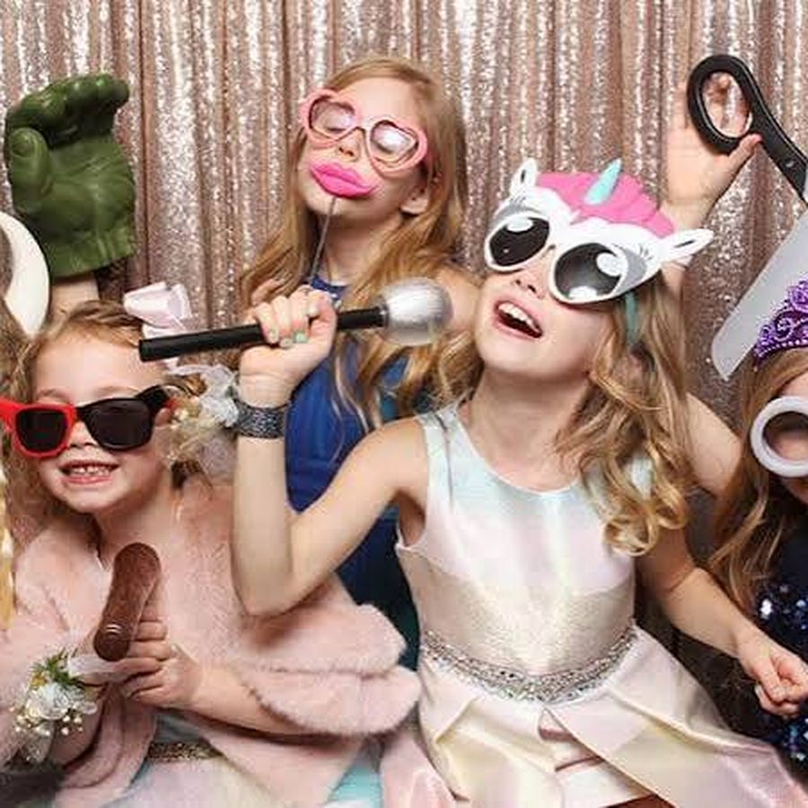 Children crowded into a photo booth in oversized glasses and props