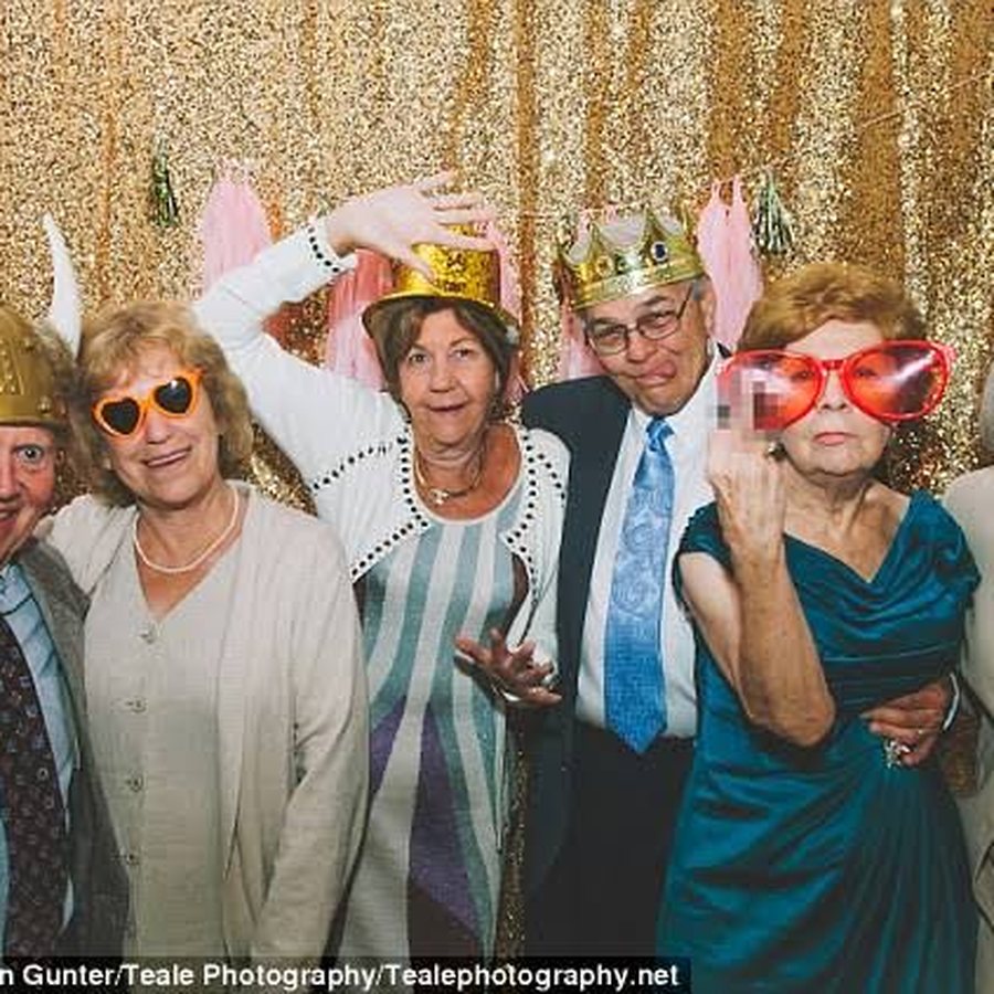 Older guests in a photo booth wearing party hats and novelty glasses